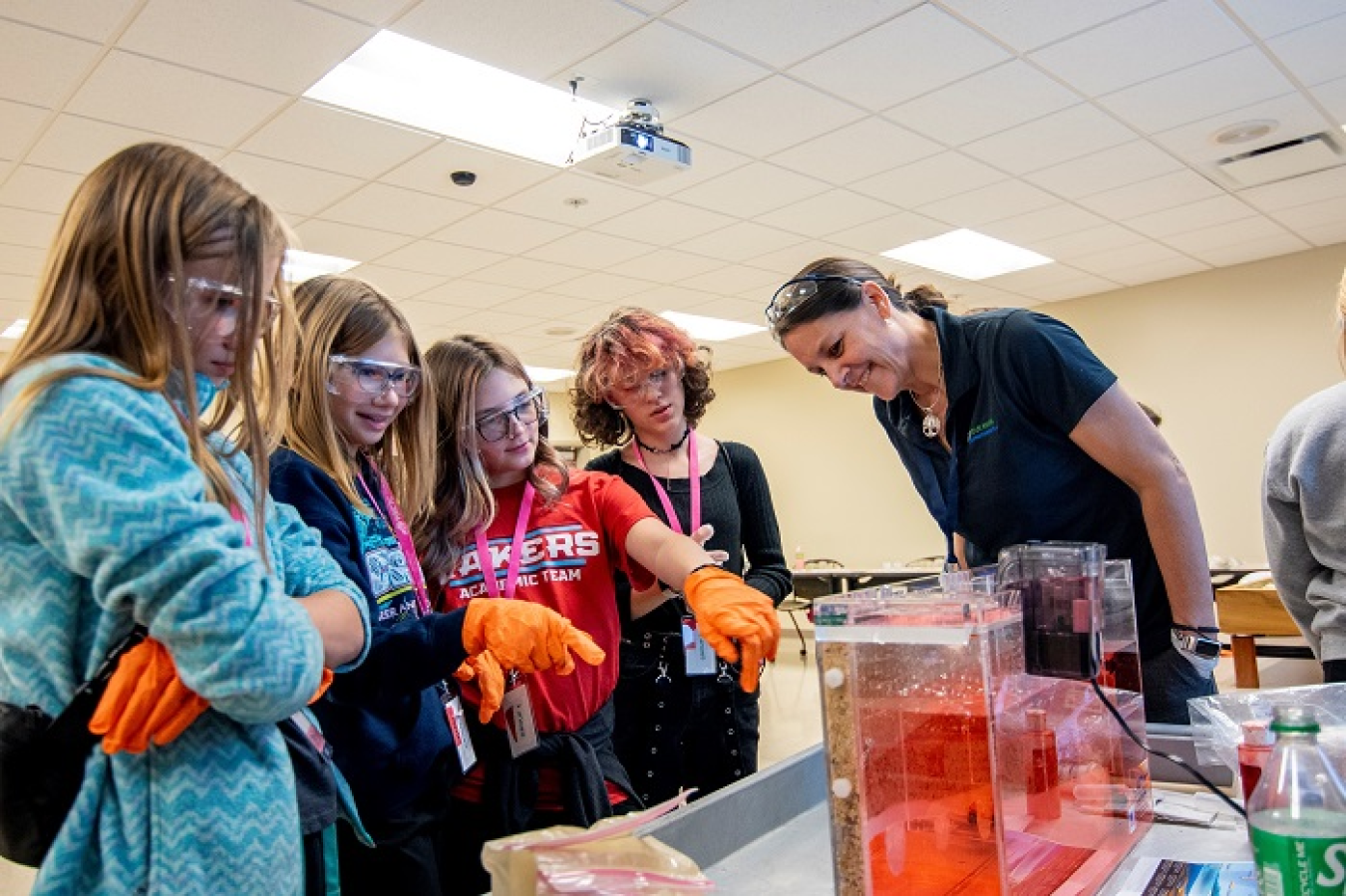 Young girls stand around a table doing science experiments with a teacher