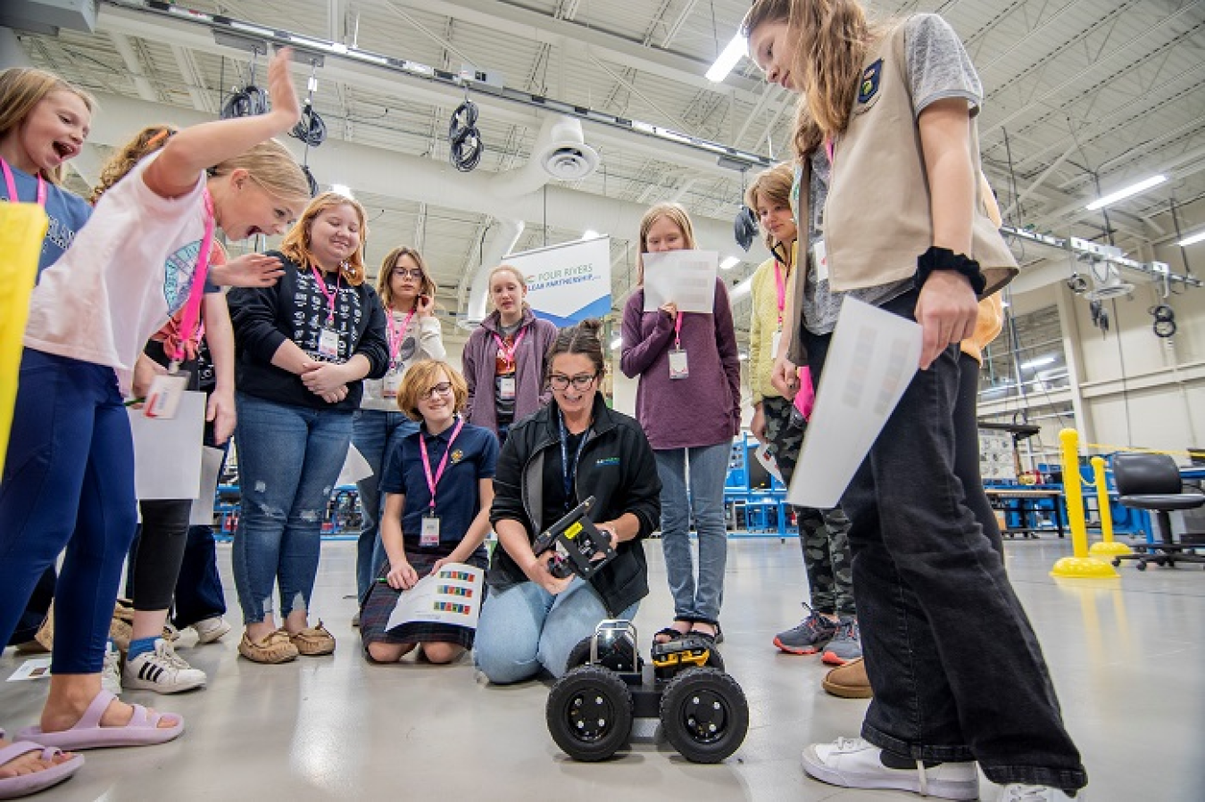 Young girls stand around a woman controlling a robot 