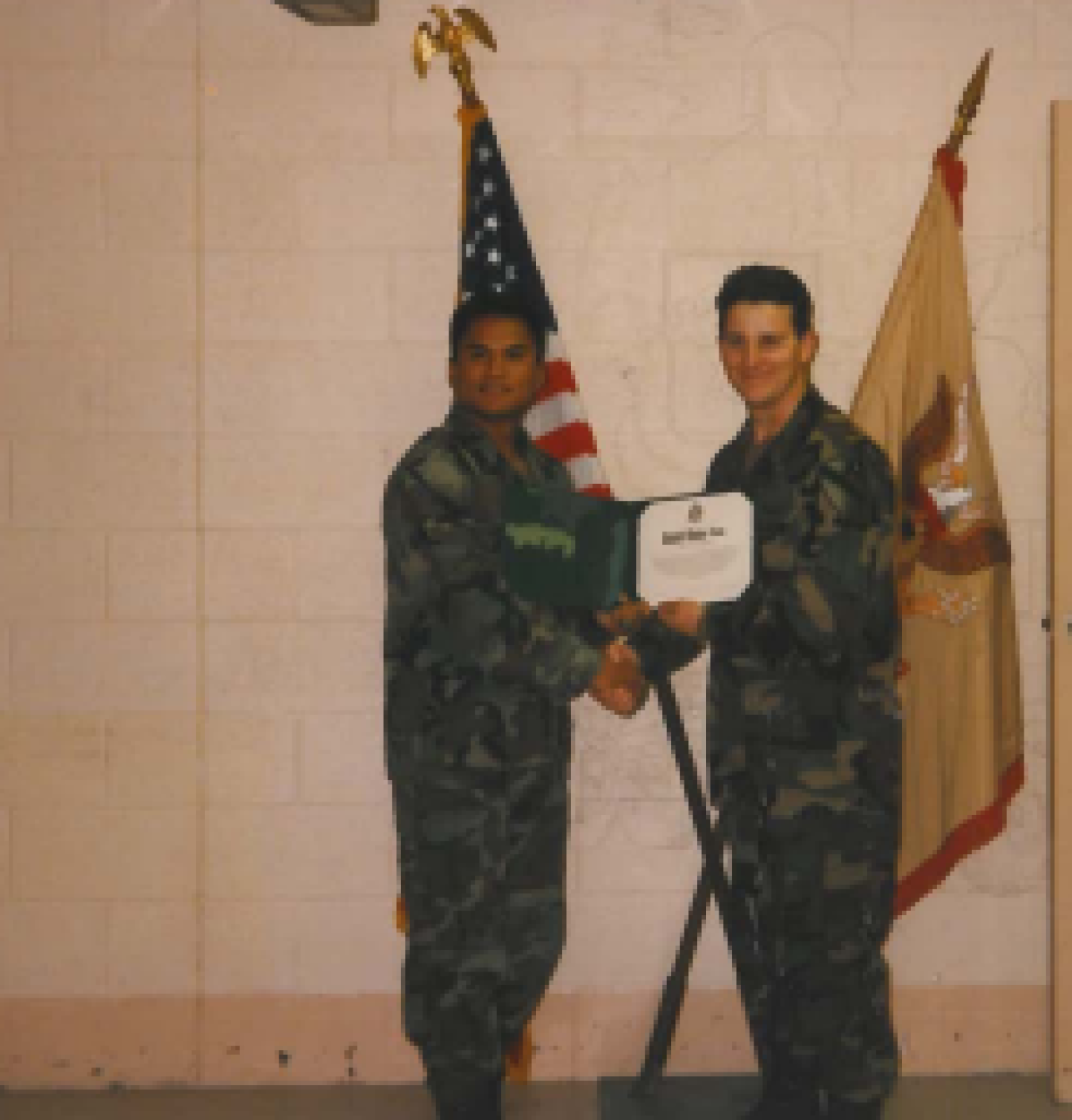 Two men in military uniforms shake hands and one is presented with a certificate