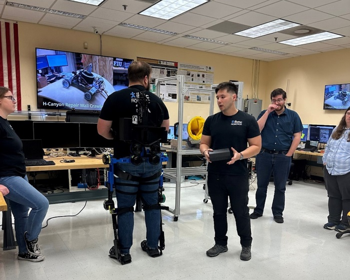 Workers stand around a table with a tv while doing a demonstration