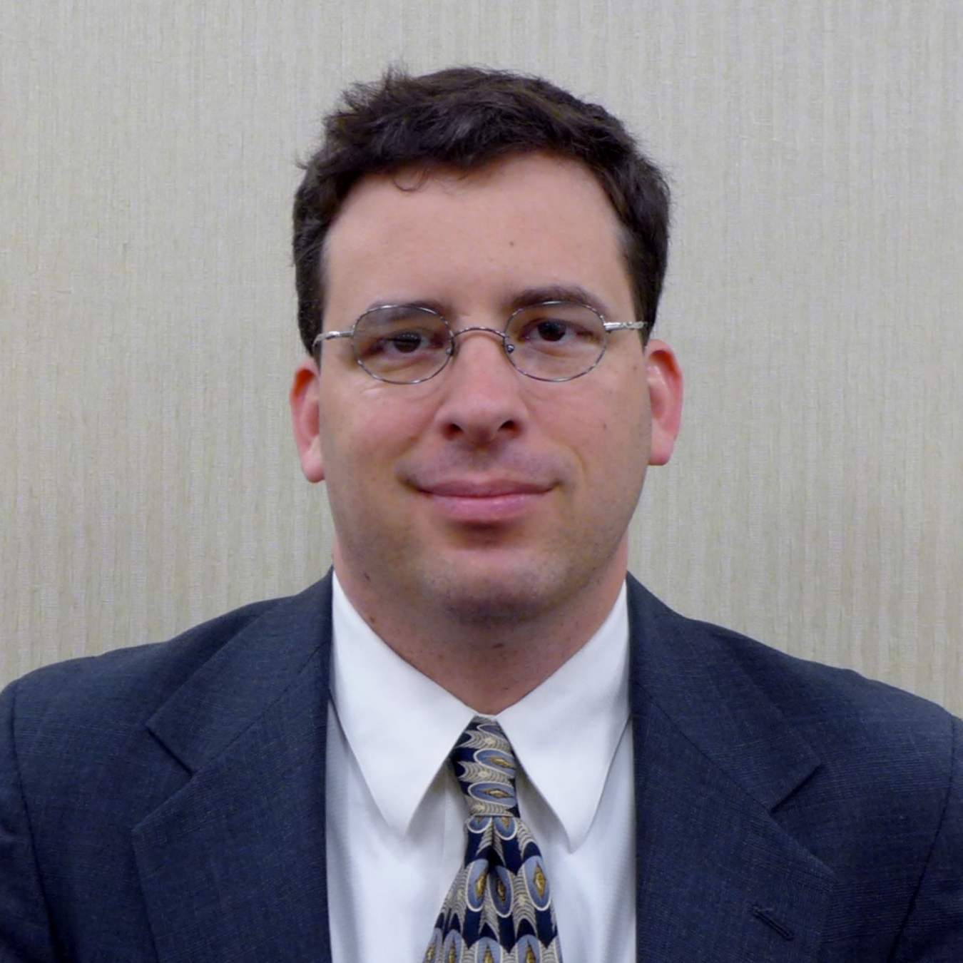 Adam Weber, smiling and wearing glasses, and a suit and tie.