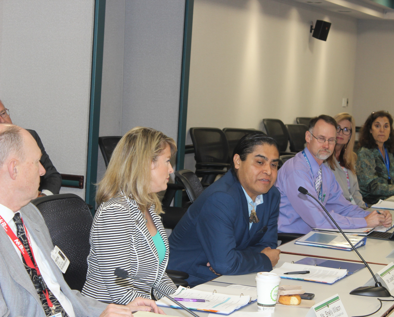 A group of four panelists sit at a table and speak into microphones