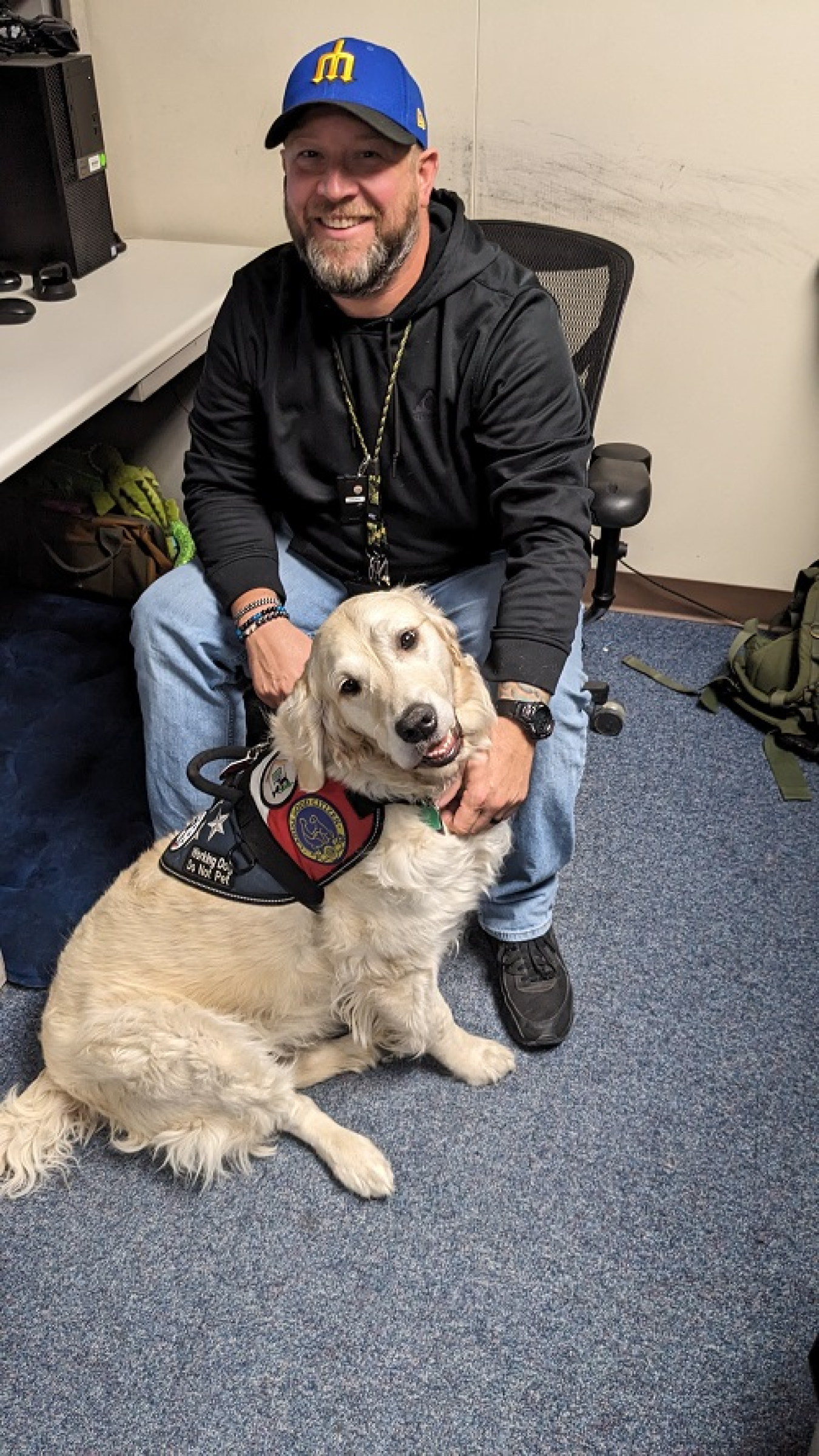 A man sits in a chair with a golden retriever service dog in front of him