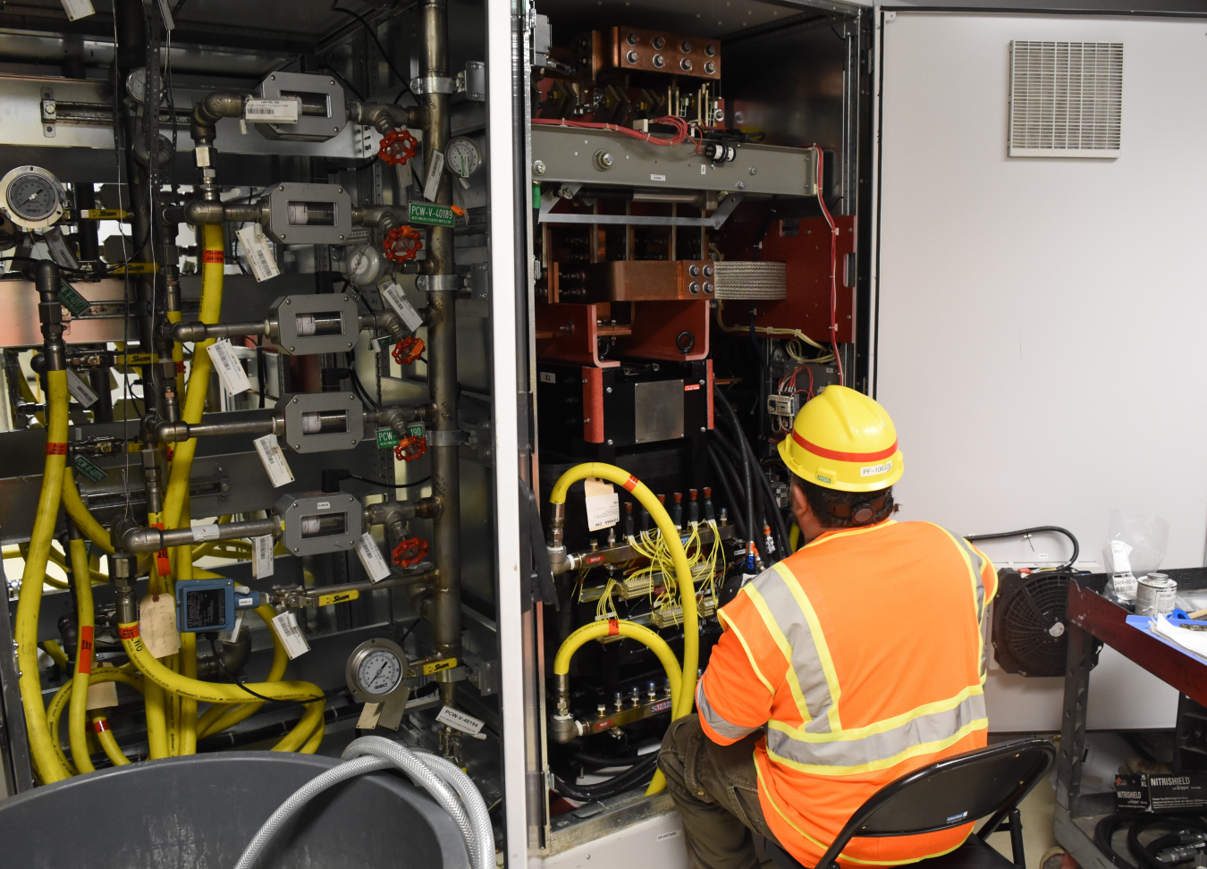 A man doing maintenance on a wall filled with wires and hoses