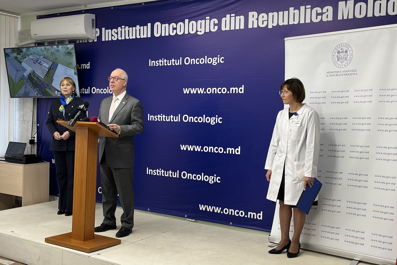 A man stands at a podium announcing news. The backdrop has a Moldovan website on it: www.onco.md.