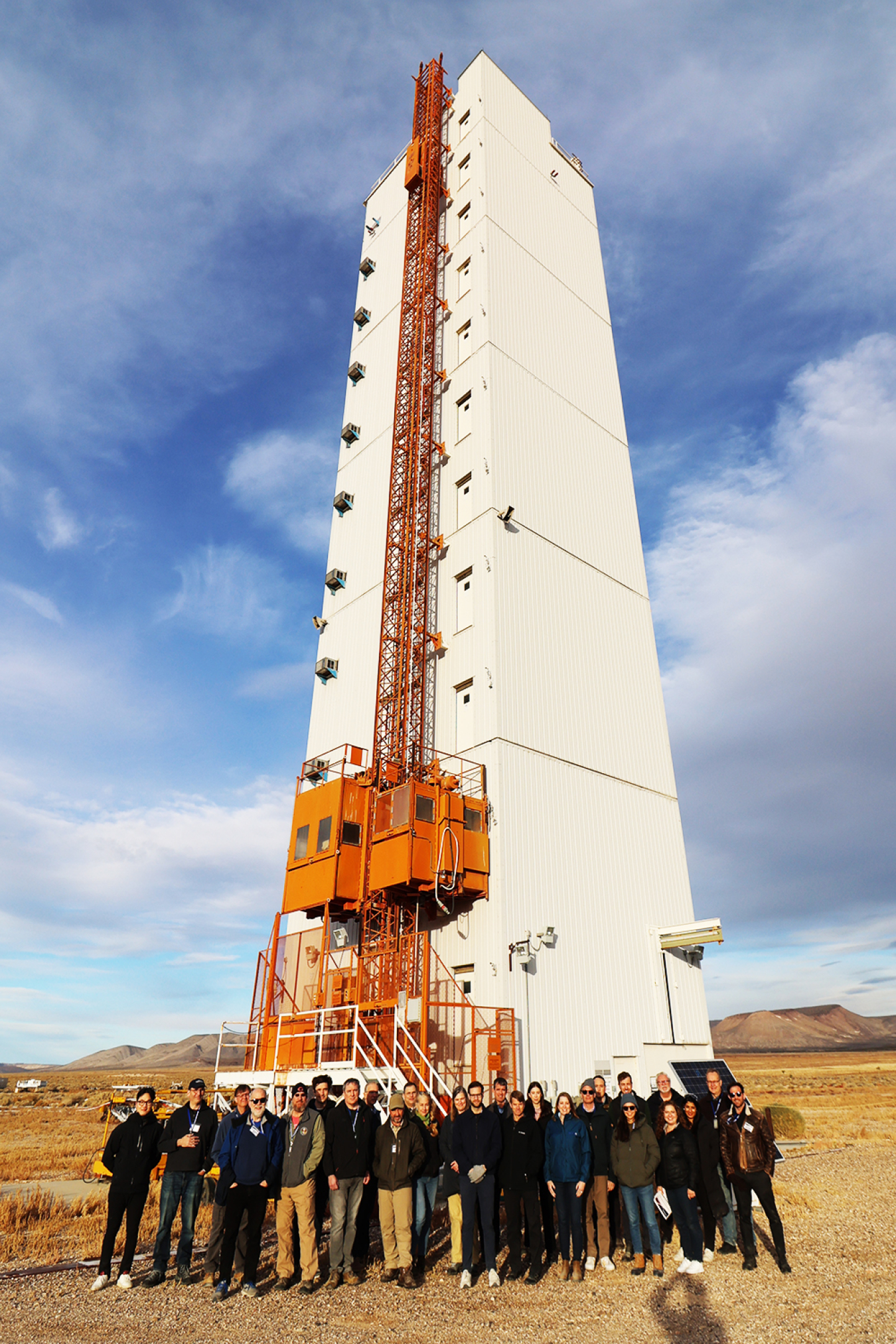 A group of people stand outside in front of a large, white tower.