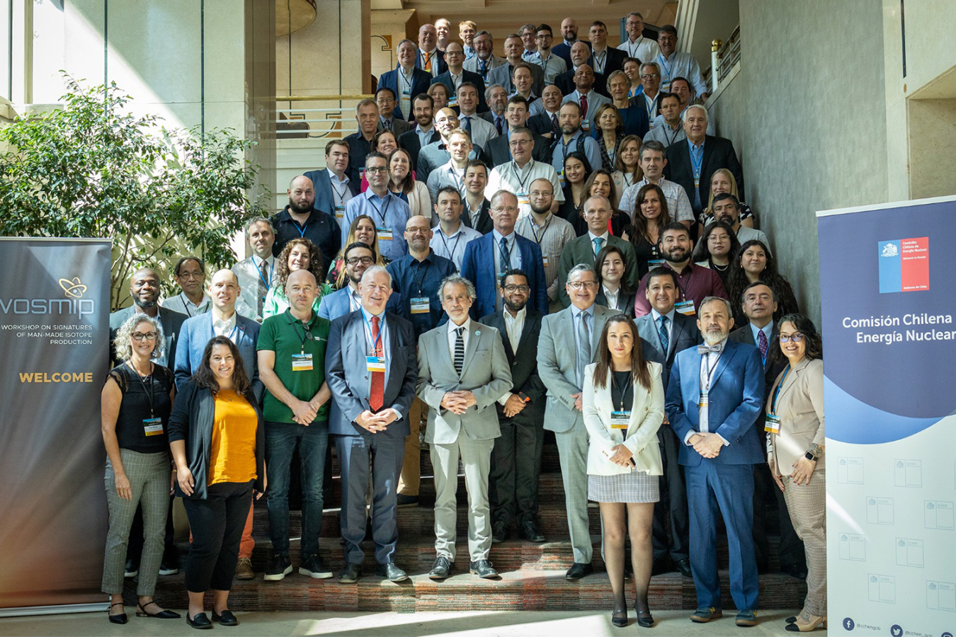 Dozens of people standing on a stairway posing for a photo. WOSMIP and Chilean Nuclear Energy Commission banners are beside them.