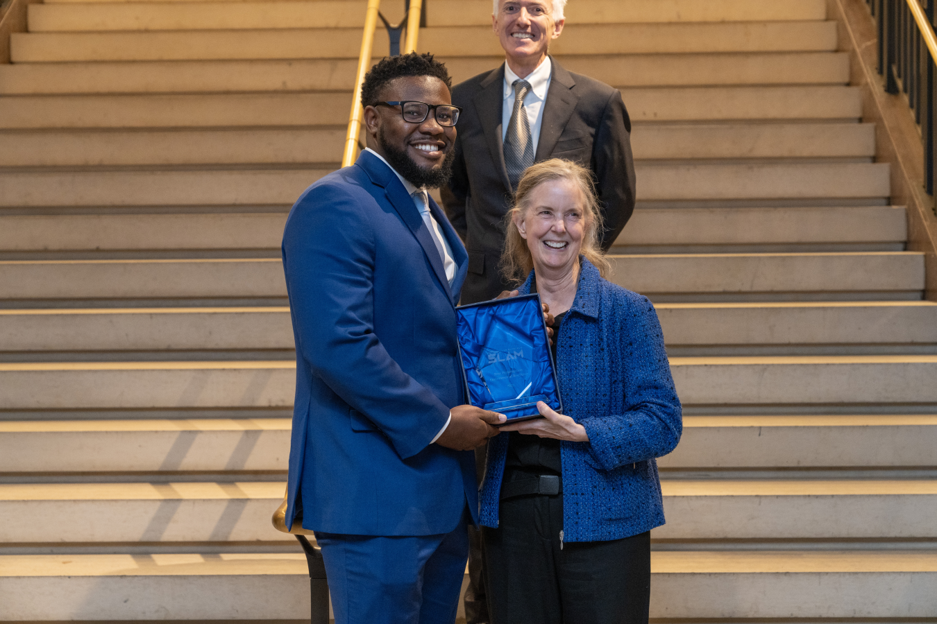 A woman presents a man with an award while they smile for a picture