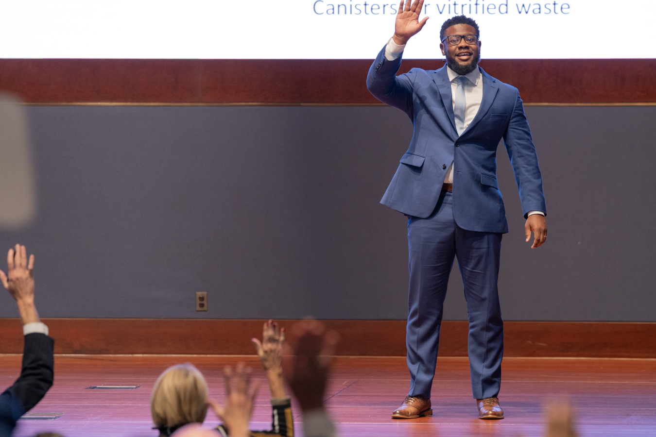 A man stands on a stage while he waves to the audience