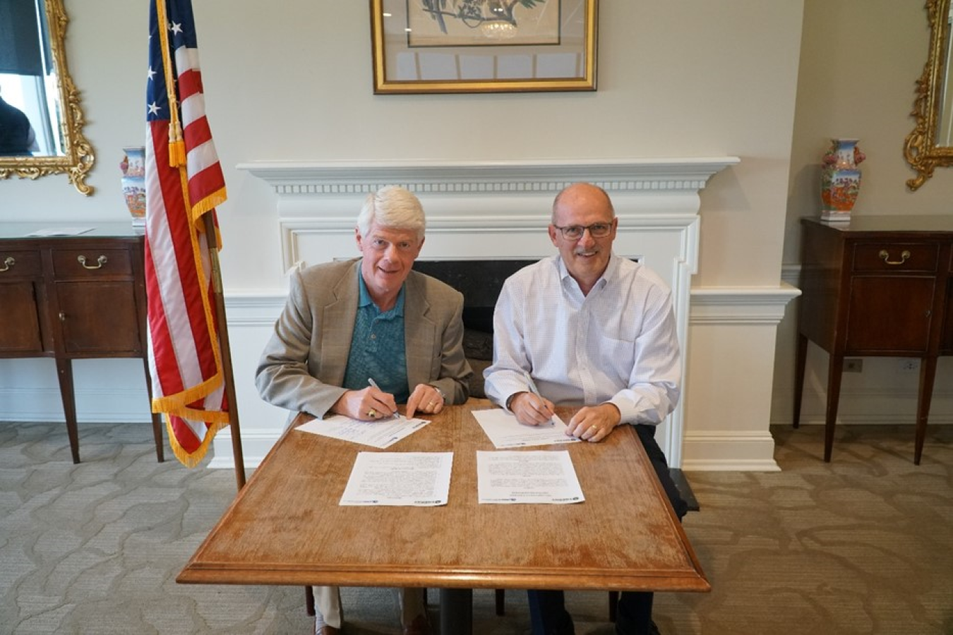 2 men sit at a table and sign papers