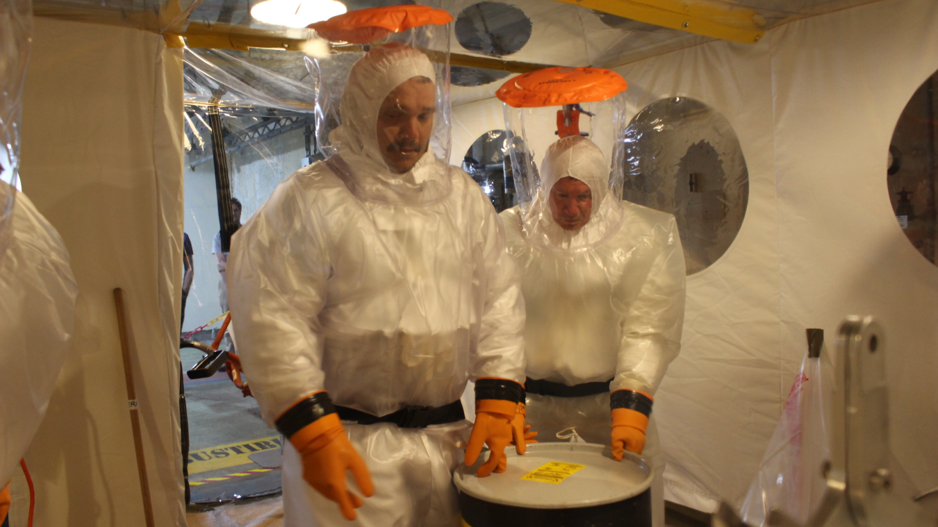 Two men in white hazmat suits stand beside a container