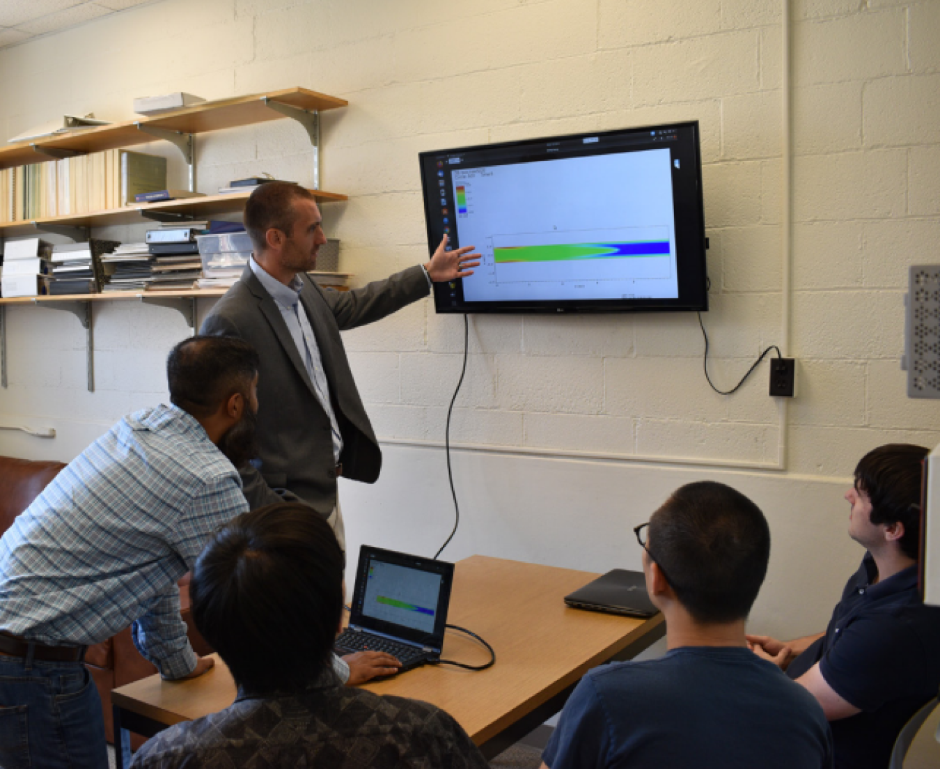 Dr. Caleb Brooks pointing to monitor while four students watch