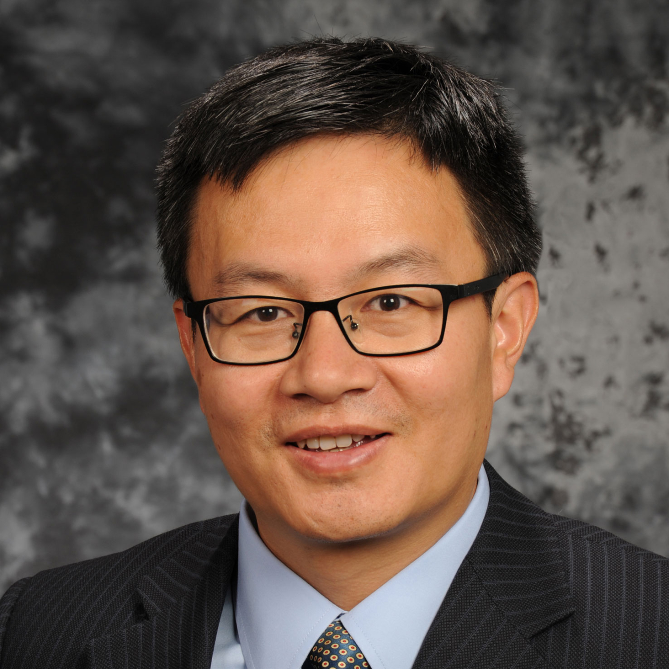 Dong Ding, smiling, wearing glasses and a suit and tie.