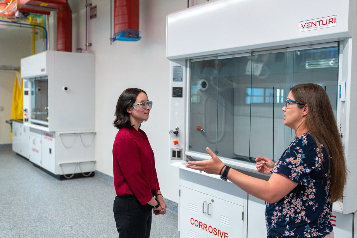 Two female scientists standing in front of lab equipment having a discussion.