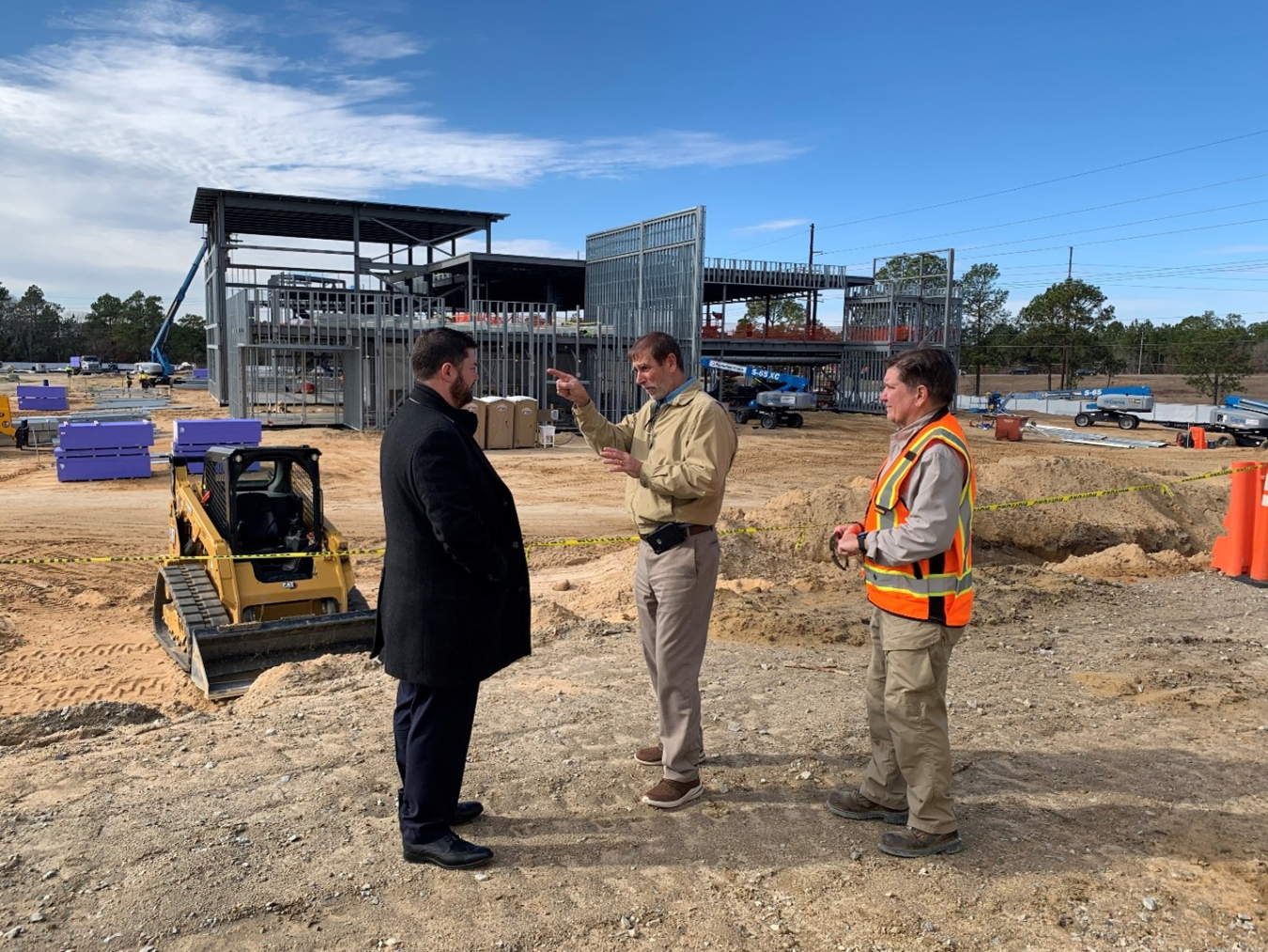 EM Official stands in the middle of a worksite and talks with 2 employees