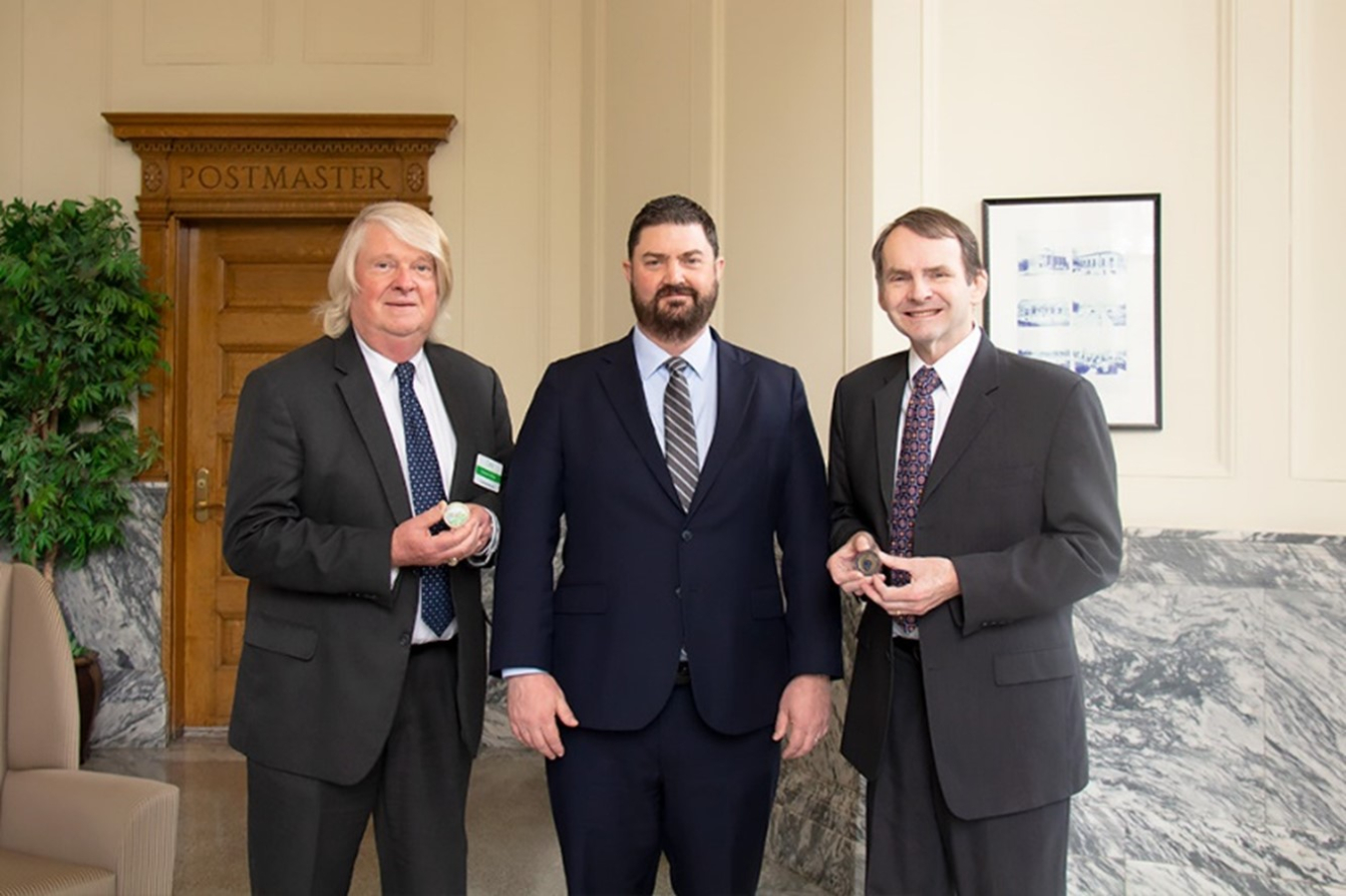 3 men in suits pose for a picture, 2 holding large coins they were awarded