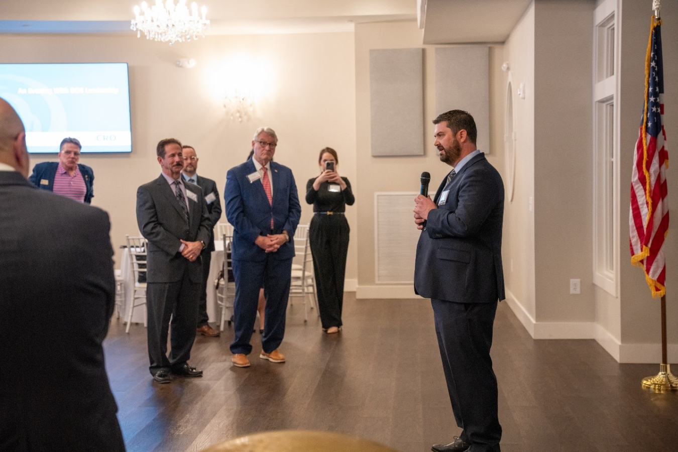 An EM leader speaks at the front of the room while people record and listen to him