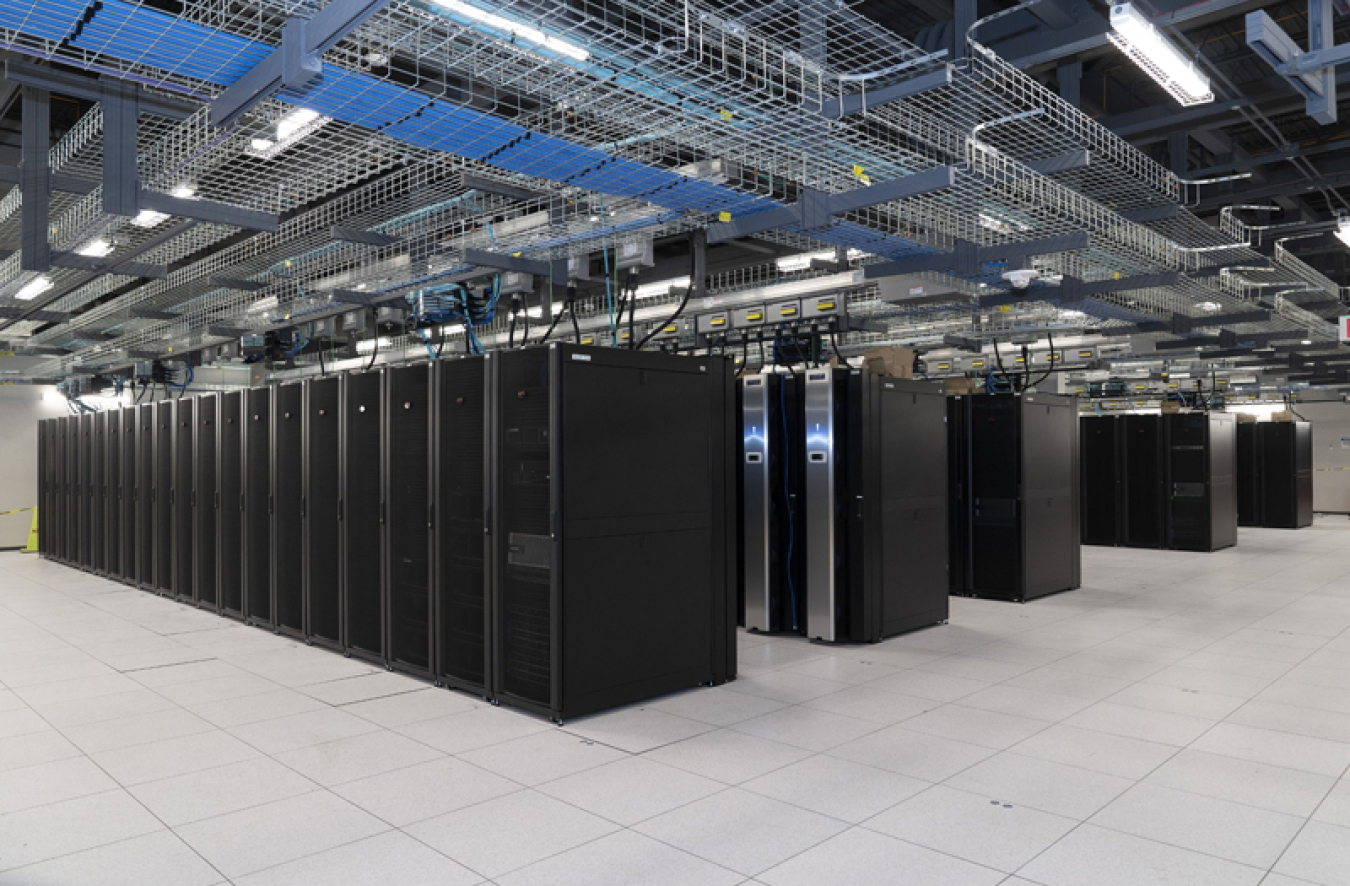 Rows of supercomputing cabinets below wire racks with electrical cords hanging down to the cabinets