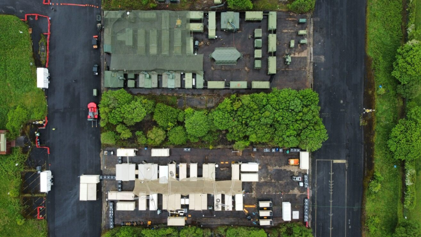 An overhead photo of several shipping containers configured as a building among bushes and trees. One set is white and the other is green.