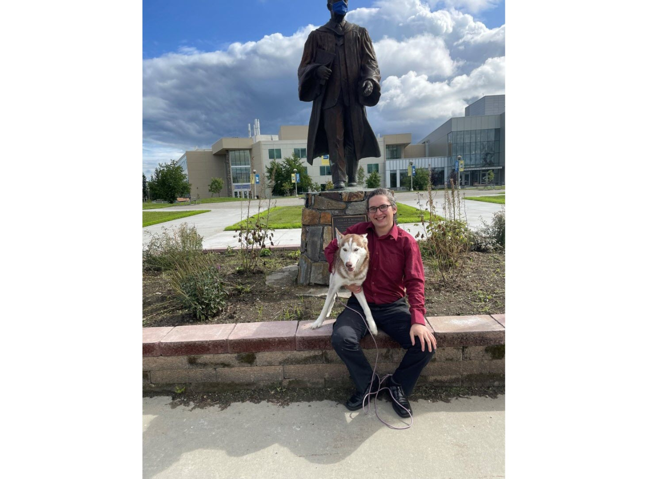 Josh Hostler hugging husky dog sitting in front of a statue 