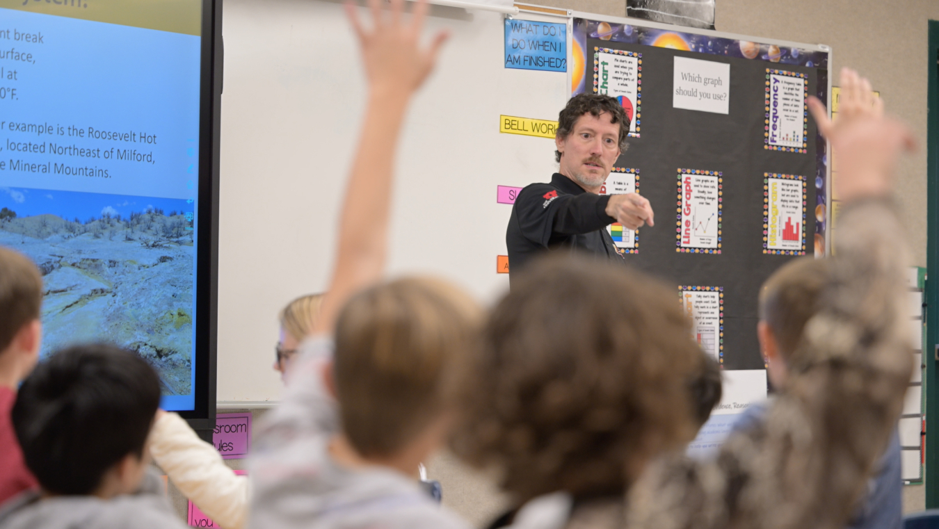 Utah FORGE staff member Christopher Katis calls on one student among many raised hands in an elementary school classroom.