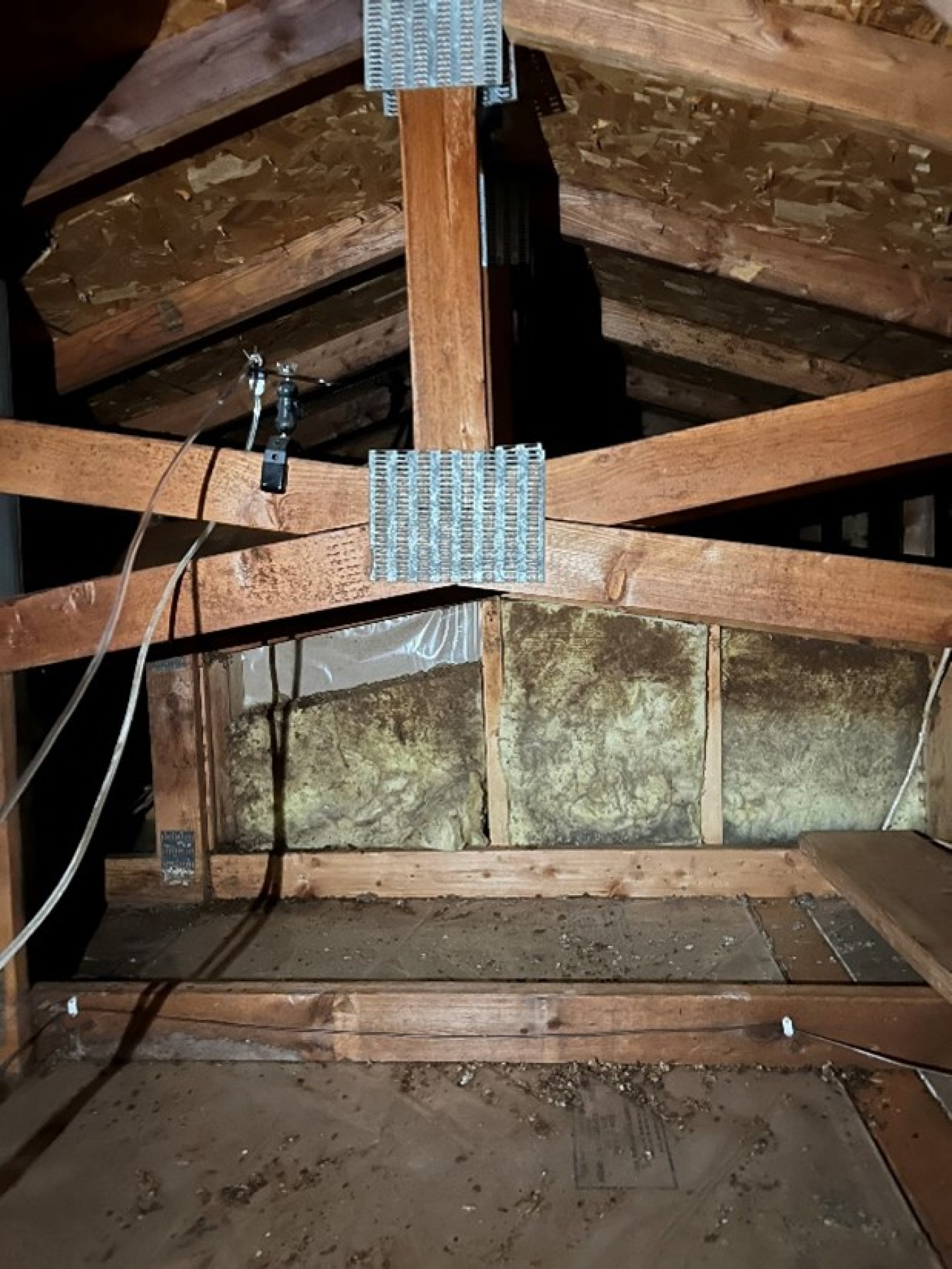 An attic, with rafters in the foreground and insulation in the background.