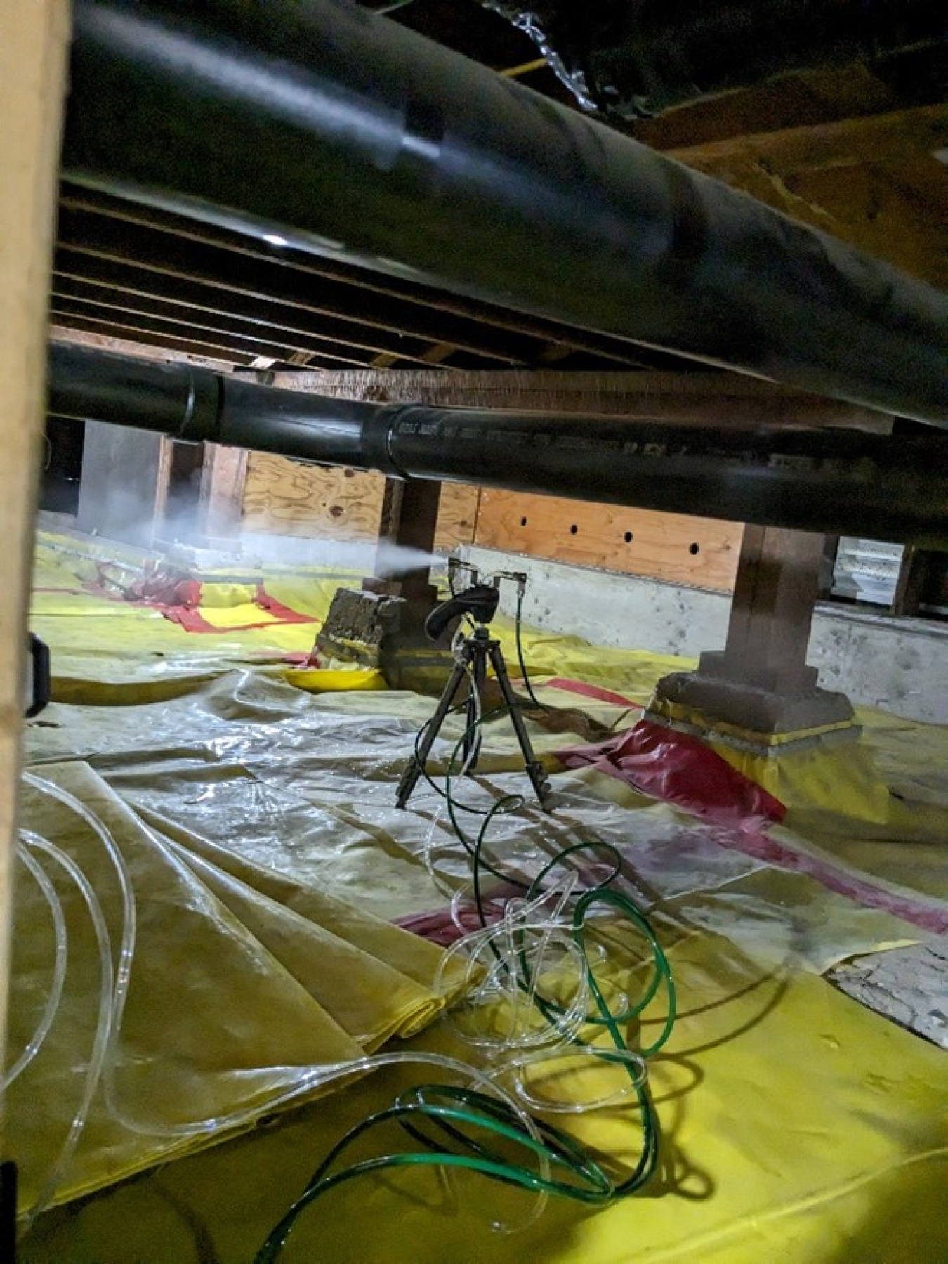 The crawlspace of a building, with air-sealing equipment around on the floor / ground.