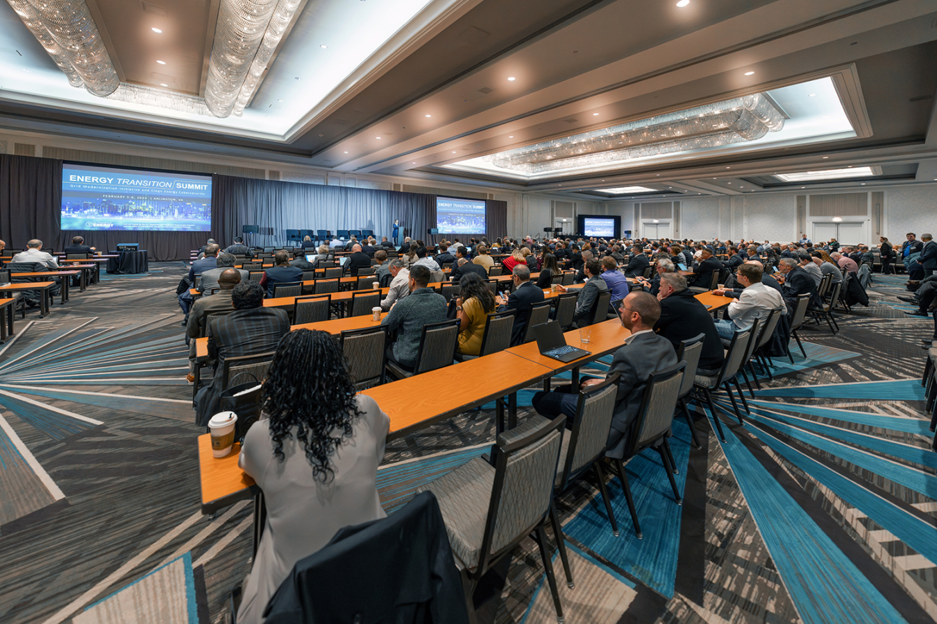 Room full of people gathered together at tables for a presentation