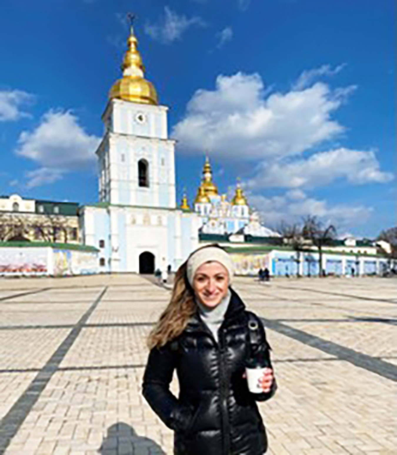 A photo of Brusilovsky in front of a golden-domed church. She is holding a cup of coffee and dressed warmly.