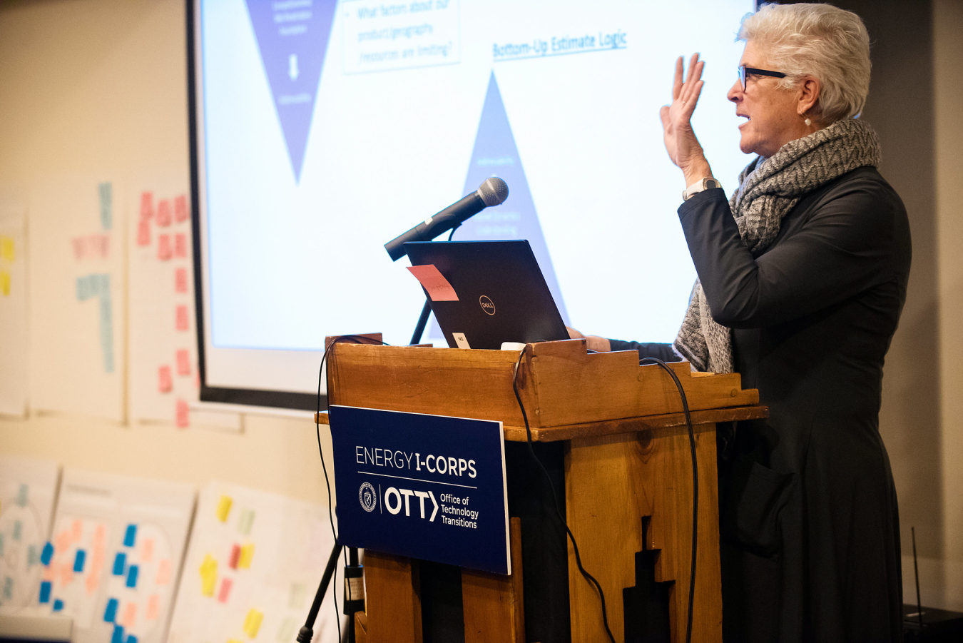 A woman presenting at a podium, speaking to an audience.