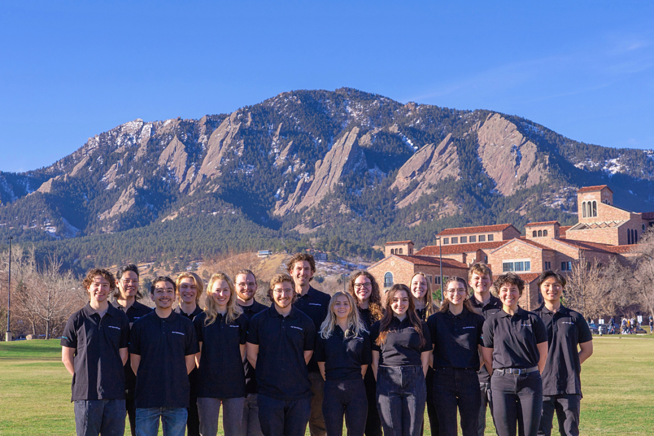 A group of people in matching shirts standing on a field in front of mountains. 