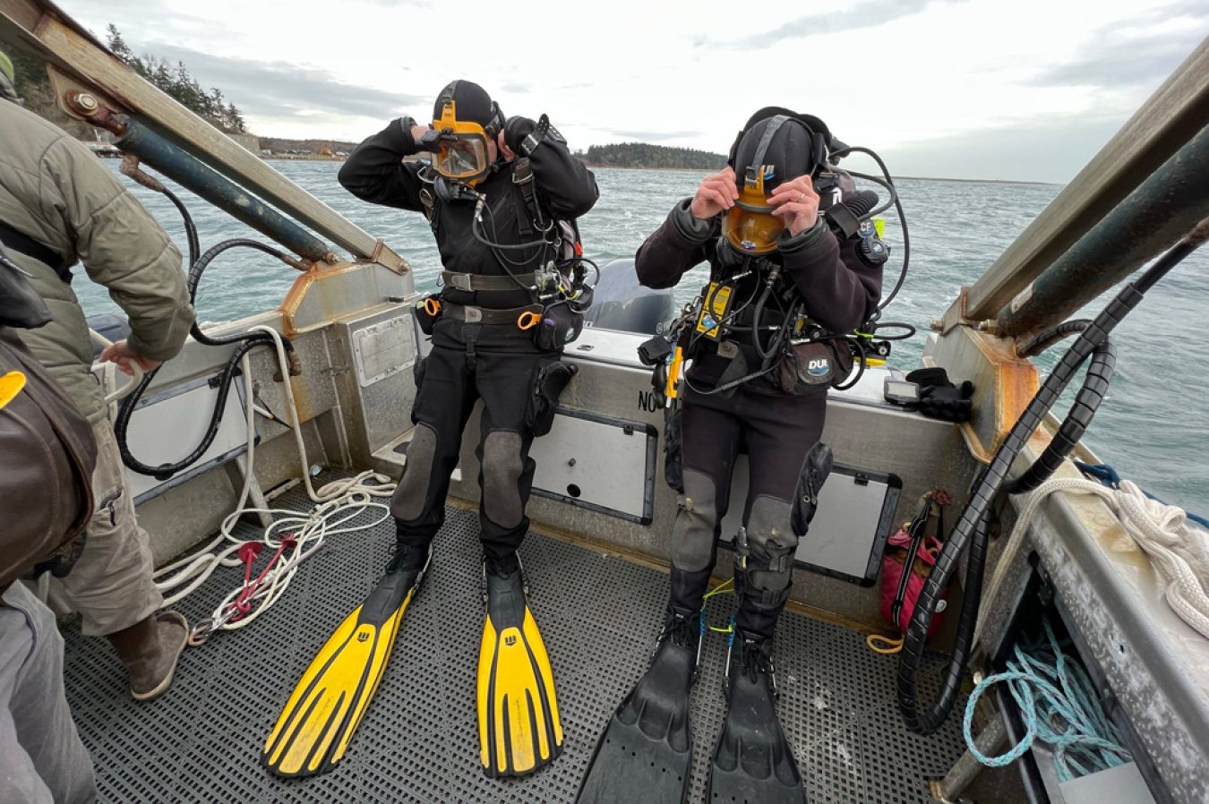 Two divers sit on a boat as they put on the last of their gear before going beneath the water to help conduct tests on underwater noise.