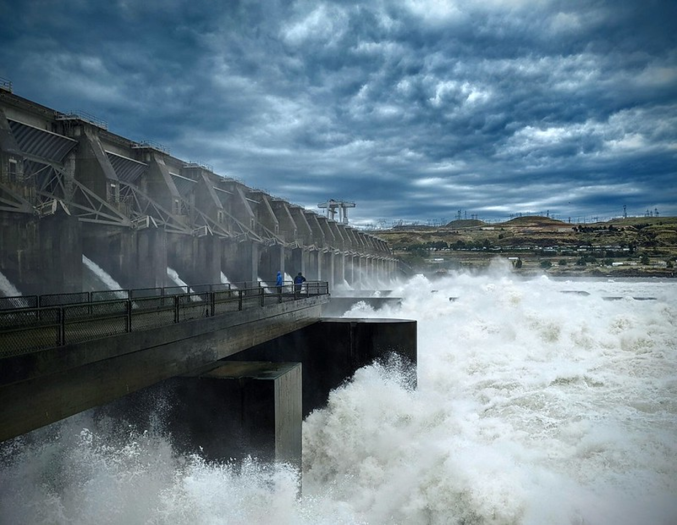 Water exits a dam’s spillway that stretches the length of a waterway. 