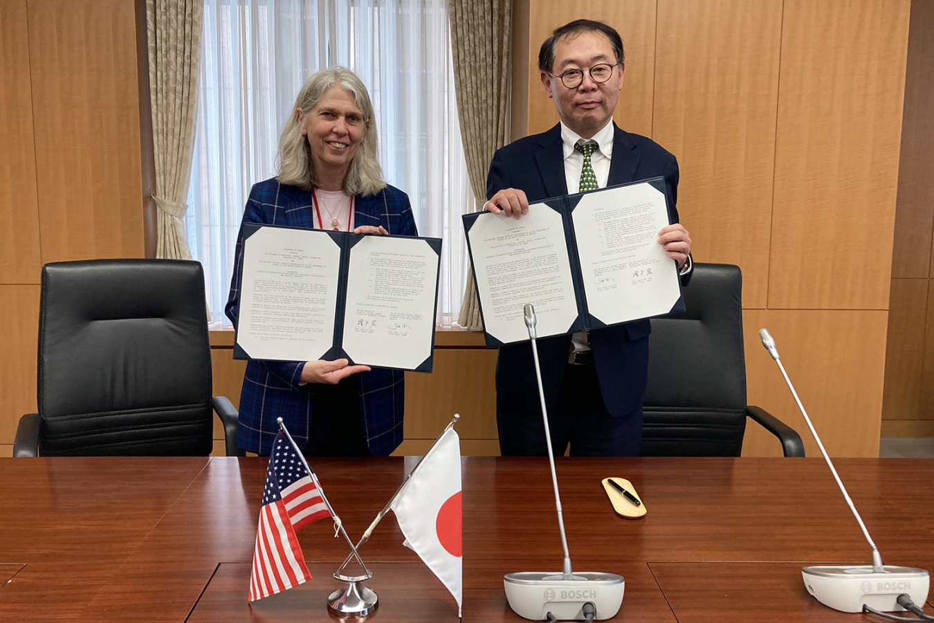 Administrator Hruby and Deputy Minister Hiroshi Masuko smile for a photo holding copies of the signed agreement. In the foreground are U.S. and Japanese flags.