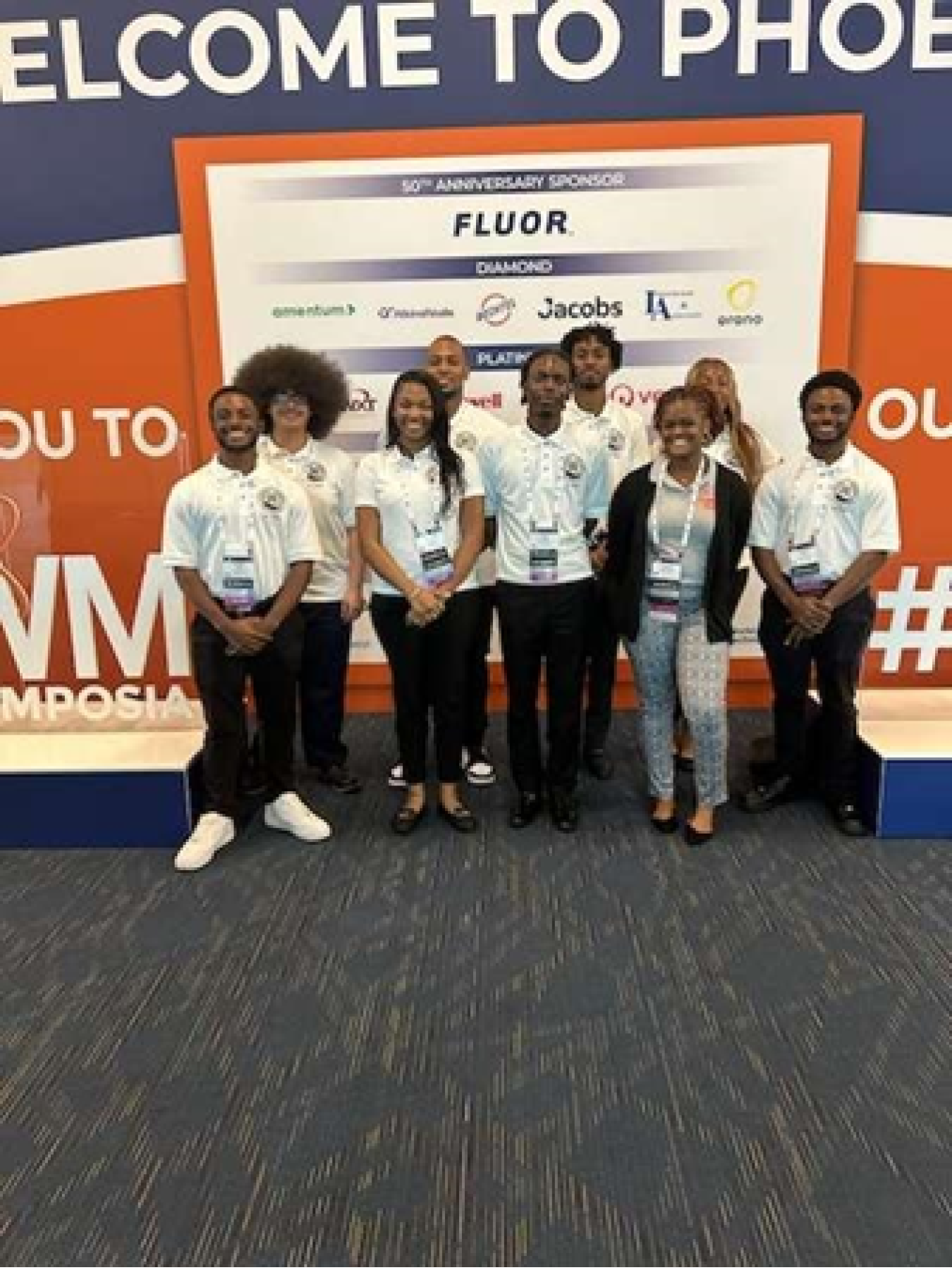 Nine young people standing beside a Waste Management Symposia sign