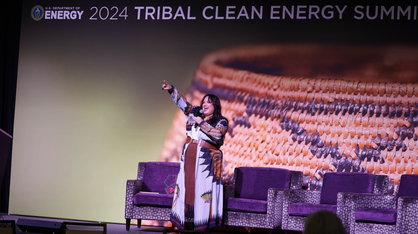 Jana Schmieding stands on stage with microphone pointing to the crowd.