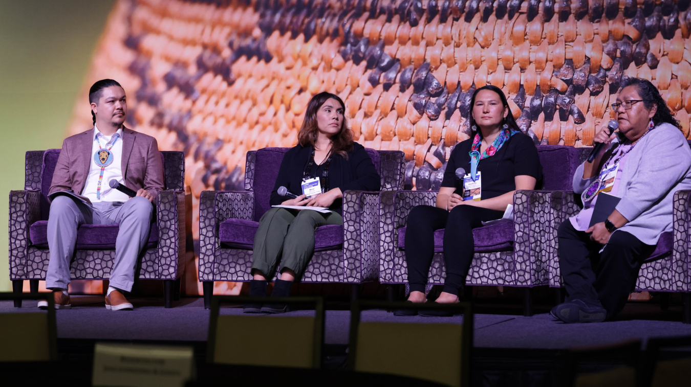 One man and three women sit on stage during a panel session.