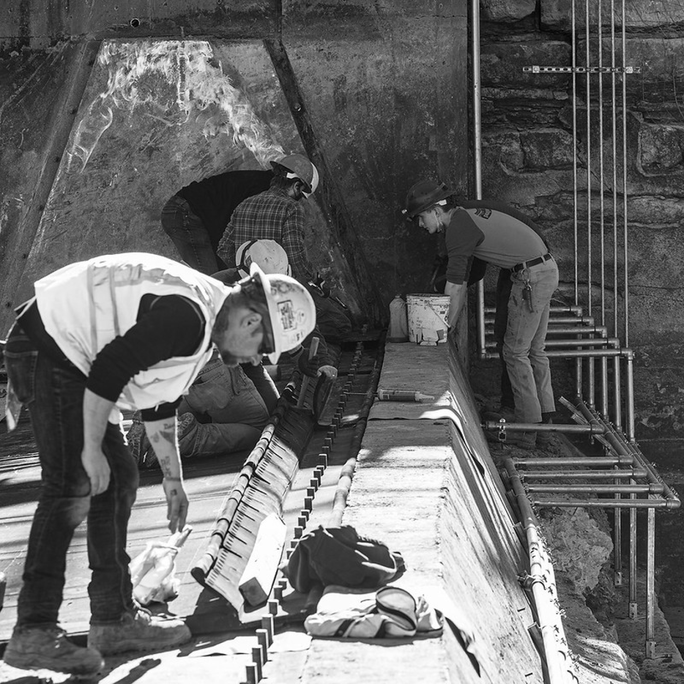 Workers lean over to view and work on a concrete structure.