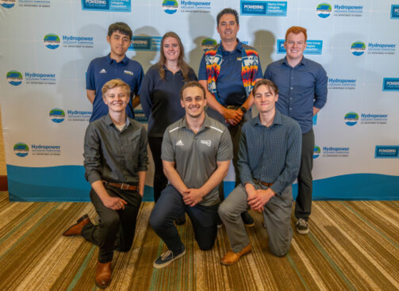 Seven people standing in front of a banner for the Hydropower Collegiate Competition.