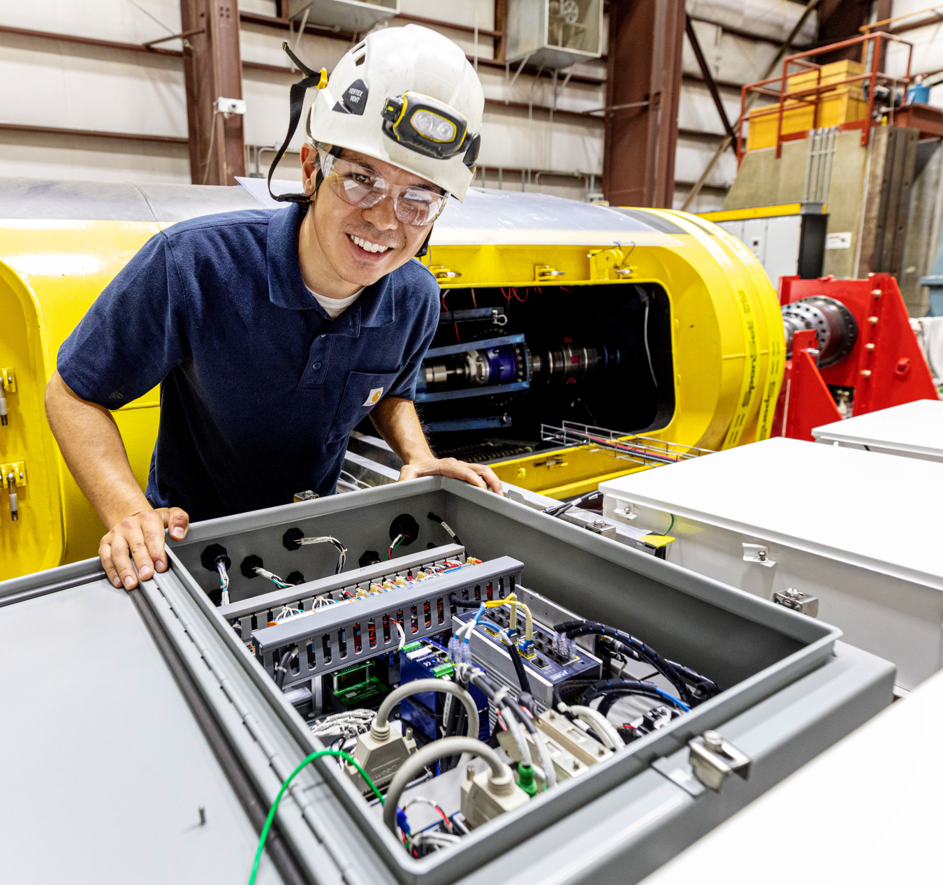 Andrew Simms leaning over an open panel housing an electrical system