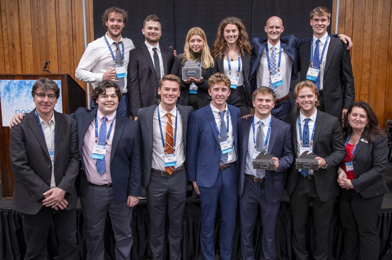 A group of people in business attire and nametags, some holding trophies