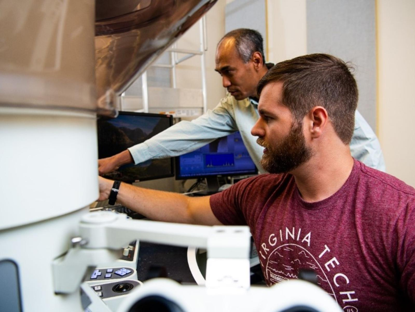 Jacob Haag and fellow researcher looking at and interacting with lab instrument.