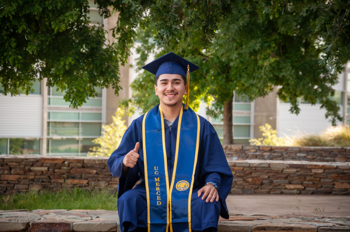 Francisco Aguirre wearing a cap and gown and giving a thumbs up