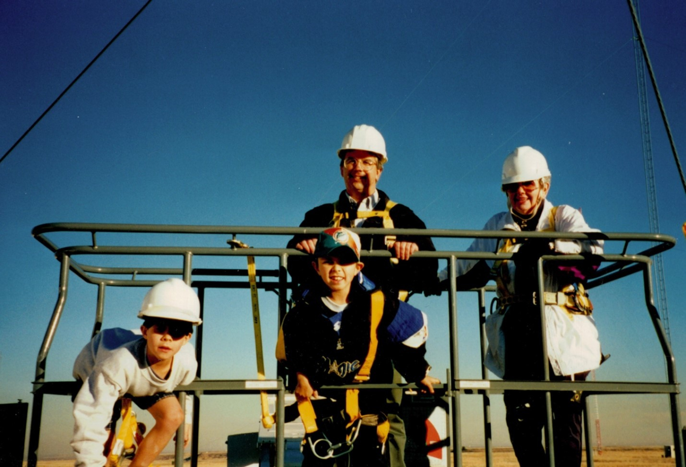 A young Andrew Simms standing on an open air elevator with two adults and another child