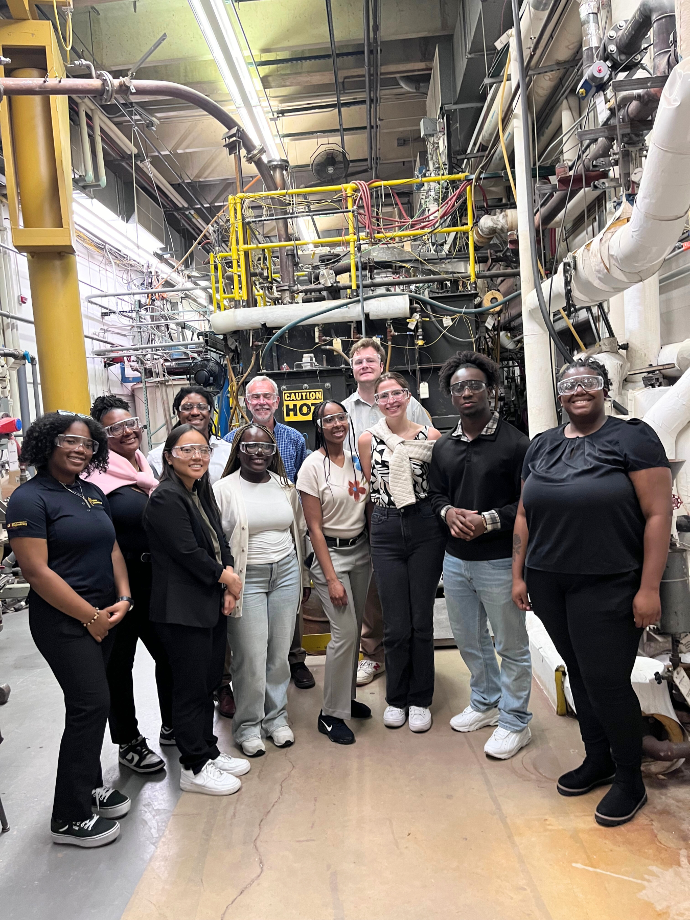 A group of young professionals wearing safety glasses pose for a group picture inside a laboratory