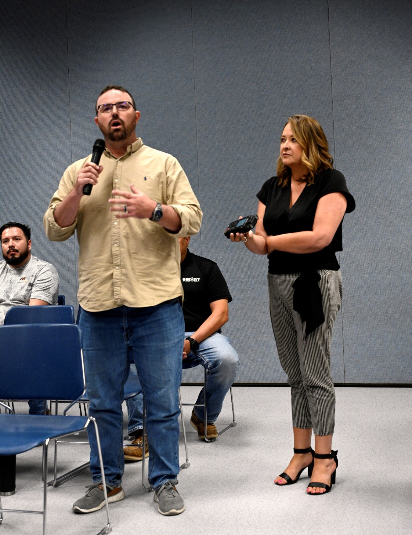 A former worker stands in the audience and asks a question to presenters with a microphone.