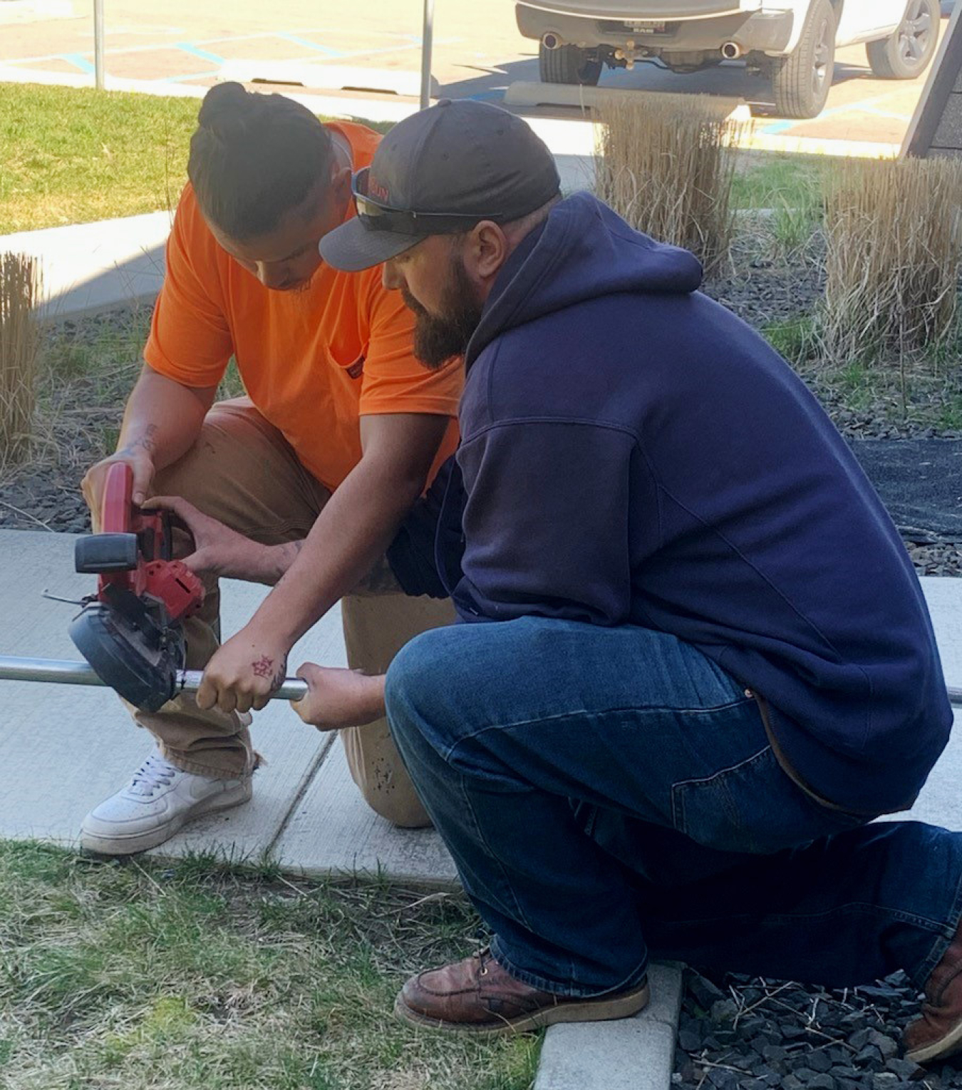 A man helps a younger man with a hand tool.