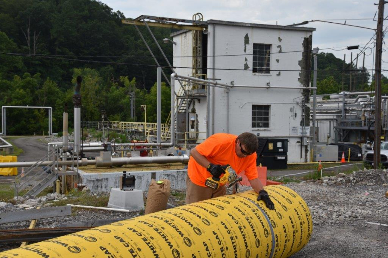 A man saws a large, yellow, tube 