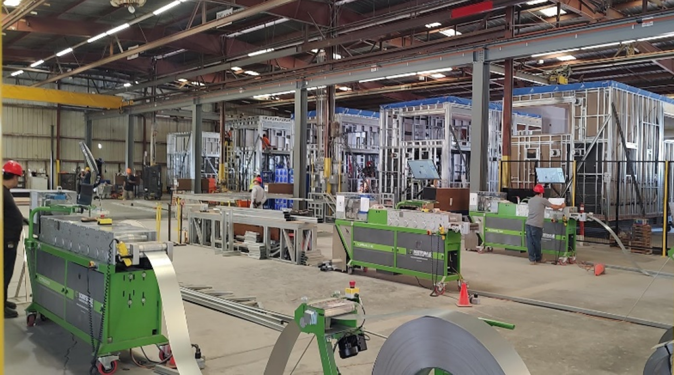 Foreground: Truss and panel machines create light-gauge steel (LGS) structural parts with exact dimensions from sheet-roll steel; Background: Under-construction LGS modular housing units.