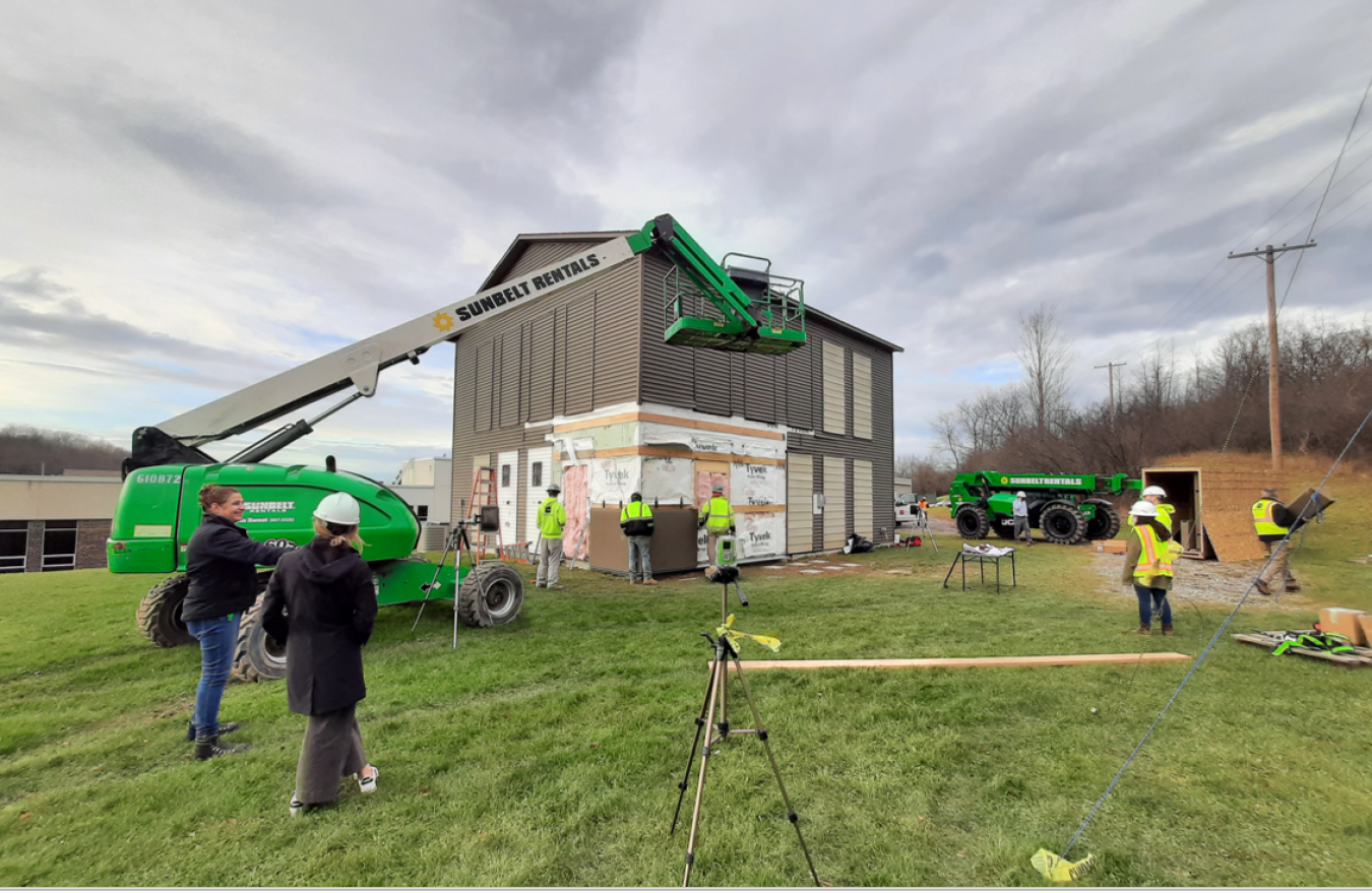 A building under construction, with workers scattered on the lawn around it.